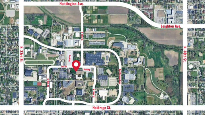Satellite map of a campus area labeled with streets and a red location marker in the center.